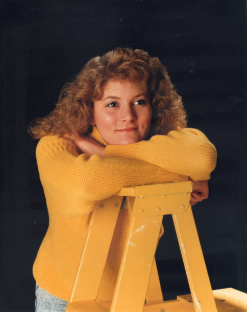 Blond teen girl with yellow sweater Girl leaning on a yellow ladder wearing a yellow sweater in a photography studio with a black background. ladder photos stock pictures, royalty-free photos & images