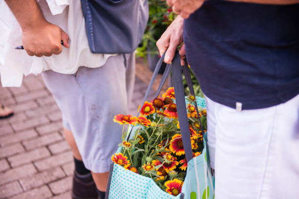 Close up of Customer Holding Bag of Flowers at the Winter Park Farmers Market This is a horizontal, color photograph of the Winter Park, Florida famers market. A customer holds a shopping bag with flowers to purchase. winter park florida stock pictures, royalty-free photos & images