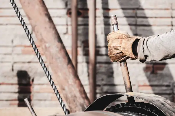 Worker hand pulling the lever of a pile driver (bate-estaca). Construction worker. Hand holding a lever. Worker hand wearing worn out gloves triggering a motor that moves steel cables.