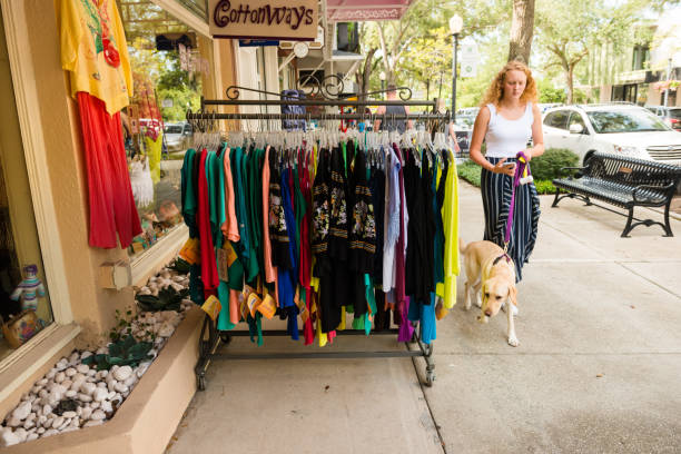 Woman with Dog Walks by Clothing For Sale at Park Avenue in Winter Park USA This is a horizontal, color photograph of a woman with a dog walking by a retail display along the sidewalk of Park Avenue in downtown Winter Park, Florida. winter park florida stock pictures, royalty-free photos & images