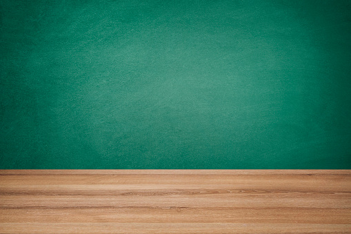 Empty school desk against green chalkboard background