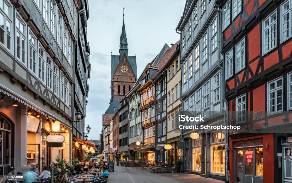 High Street in Hannover's Aldstadt at dusk Hannover's historical city center. Half-timbered houses of Kramerstrasse (huckster street) with Marktkirche (market church) in the background. Moody light at dusk. Houses are already illuminated. Germany - Europe Hanover - Germany Stock Photo