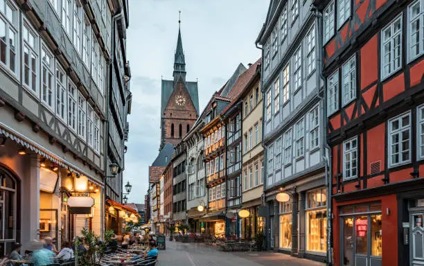 Hannover's historical city center. Half-timbered houses of Kramerstrasse (huckster street) with Marktkirche (market church) in the background. Moody light at dusk. Houses are already illuminated. Germany - Europe