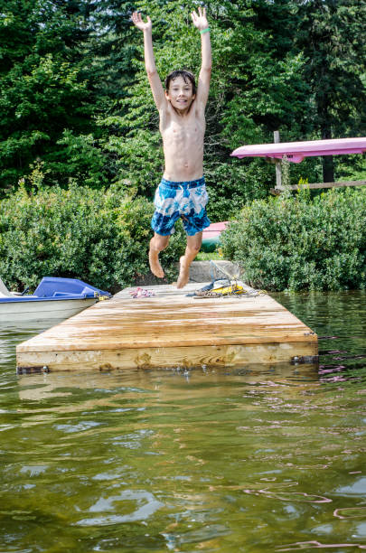 istock Young boy jumping in a lake from the pier during summer day 1030485280