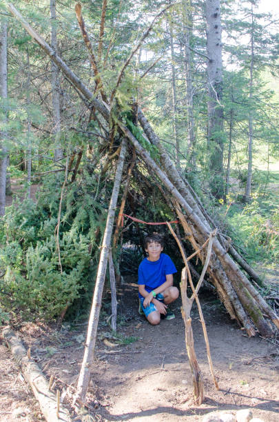 Young boy inside his wooden hut he made in the forest during summer day Young boy inside his wooden hut he made in the forest during summer day sheltering photos stock pictures, royalty-free photos & images