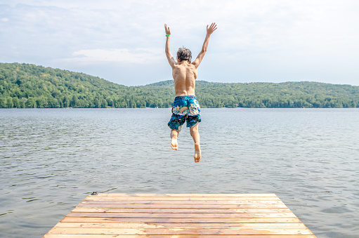 Young boy jumping in a lake from the pier during summer day