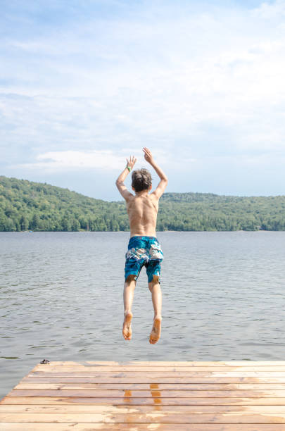 istock Young boy jumping in a lake from the pier during summer day 1030492946