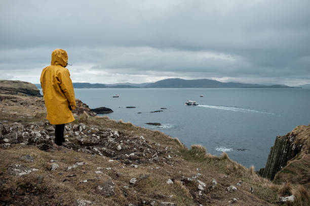 Woman with yellow oilskin jacket observing a boat from Staffa Island stock photo