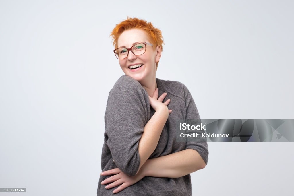 Pretty caucasian mature woman with short red hairstyle in simple pulover is shy to hear a compliment. Pretty caucasian mature woman with short red hairstyle in simple pulover is shy to hear a compliment. I'm a little confused by your attention. Mature Women Stock Photo