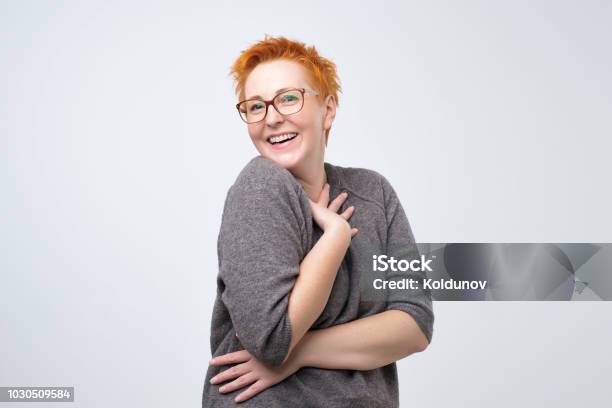 Pretty Caucasian Mature Woman With Short Red Hairstyle In Simple Pulover Is Shy To Hear A Compliment Stock Photo - Download Image Now