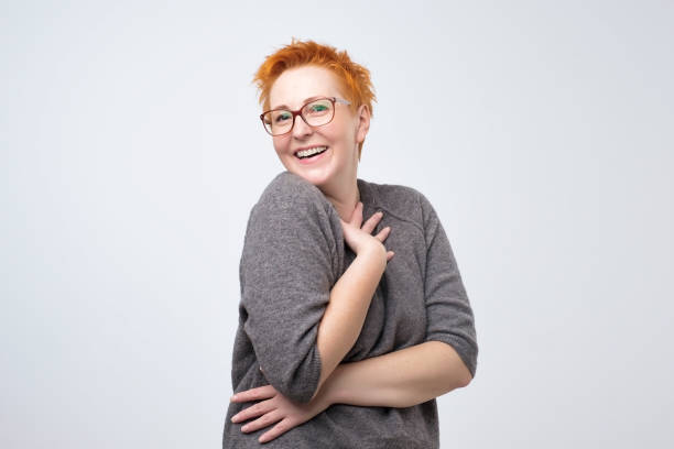 mulher madura muito caucasiana com penteado vermelho curto em pulover simples é tímida para ouvir um elogio. - gesturing facial expression women human face - fotografias e filmes do acervo