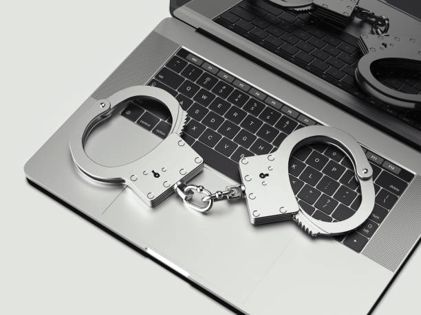 istock Close up of handcuffs on laptop isolated on white background, 3d rendering. 1030509846