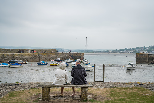 Marazion, England -  May 2018 : Old couple sitting on a bench by the marina in front of St Michaels Mount,  Cornwall, England