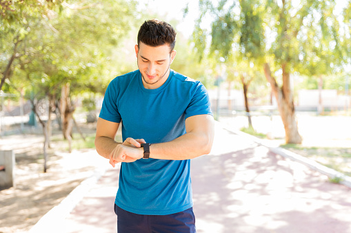 Athletic young man checking step counts on smart watch in park during sunny day