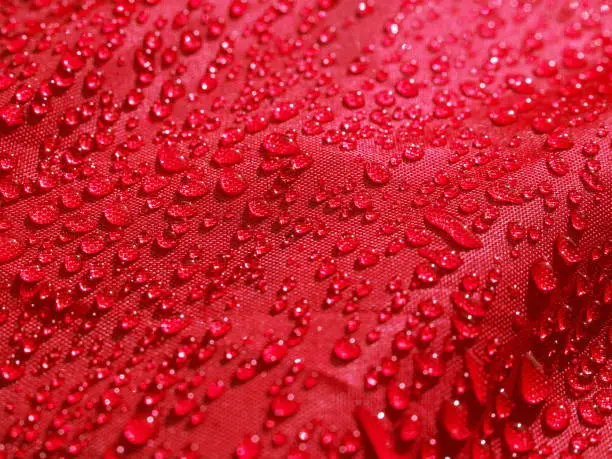 Photo of Red waterproof fabric with waterdrops close up