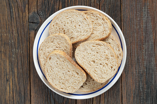 Slices of wheat bread with bran in a plate on old wooden background, top view