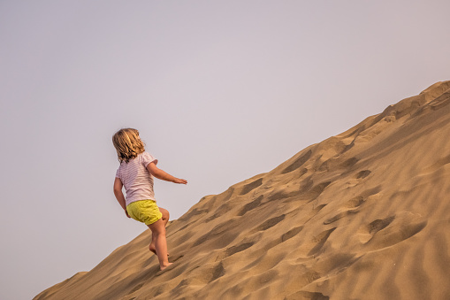 Little girl walking up the sand on the sand dunes in  the Natural Reserve of Dunes of Maspaloma in Gran Canaria