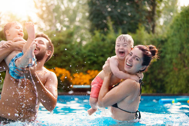 little boy with down syndrome having fun in the swimming pool with his family - swimming child swimwear little boys imagens e fotografias de stock