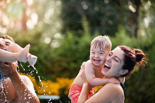 Three years old Little boy with Down syndrome having fun in the swimming pool with his family. His uncle holds him in his arms. His mother holds her two-year-old brother in her arms. Color and horizontal Photo was taken in Quebec Canada.