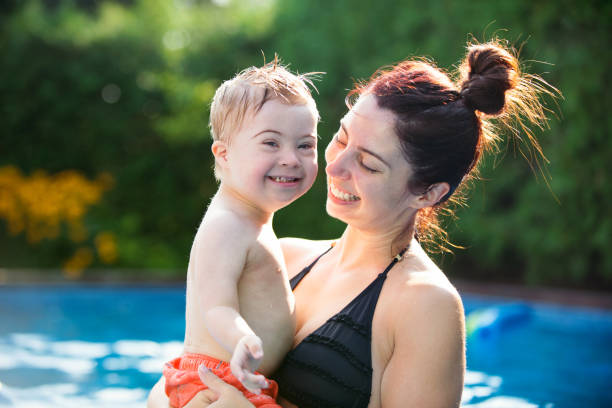 little boy with down syndrome having fun in the swimming pool with his family - swimming child swimwear little boys imagens e fotografias de stock