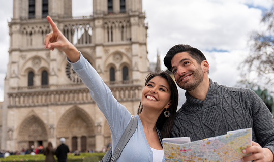 Portrait of a loving couple sightseeing in Paris vising Notre-Dame and using a map while pointing away