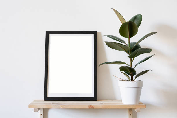 istock Poster in black frame in white stylish modern interior on a wall above green sofa. Design template mockup. 1030562878