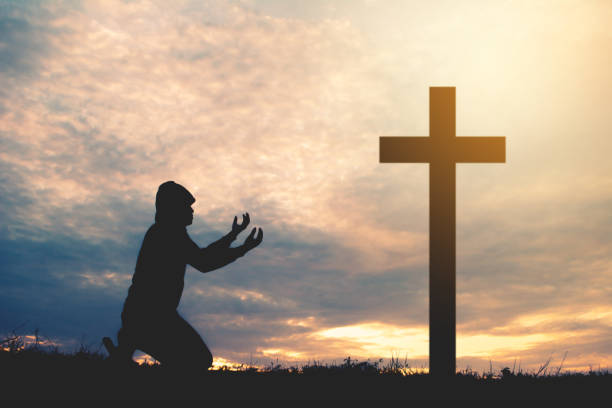 istock Silhouette Man Kneeling By Cross On Field Against Sky During Sunset 1030579914