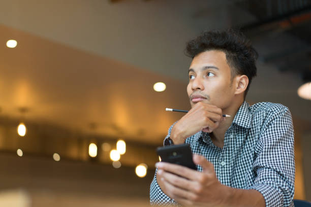 close up candid on freelance asian man looking for searching idea or thinking something with hand holding smartphone at cafe , lifestyle concept