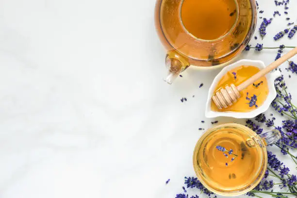 lavender tea in a cup and teapot with honey and fresh flowers over white marble table. herbal drink. top view with copy space