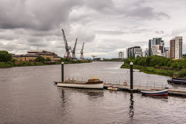 Glasgow, Scotland, UK - June 17, 2012: Looking down River Clyde from quay at Riverside Museum shows gray water, heavy cloudscape, highrises and cranes of harbor.