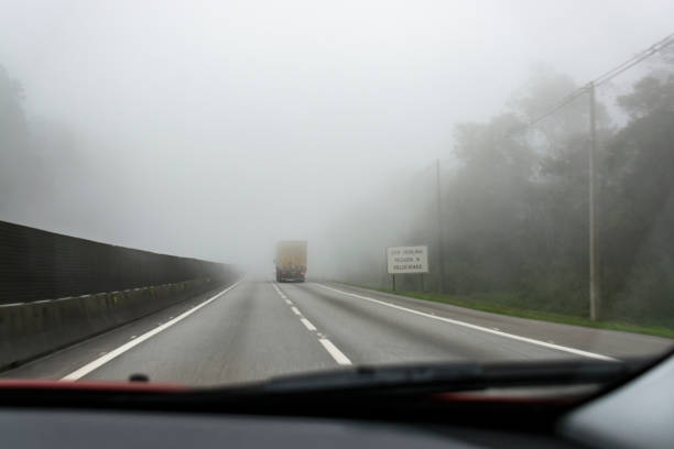 Truck traveling on road with fog and passing next to sign plate "UNDER FOG REDUCES THE SPEED" ("sob neblina reduza a velocidade") stock photo