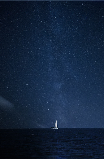 Composite image of white sailed boat on the horizon with night sky