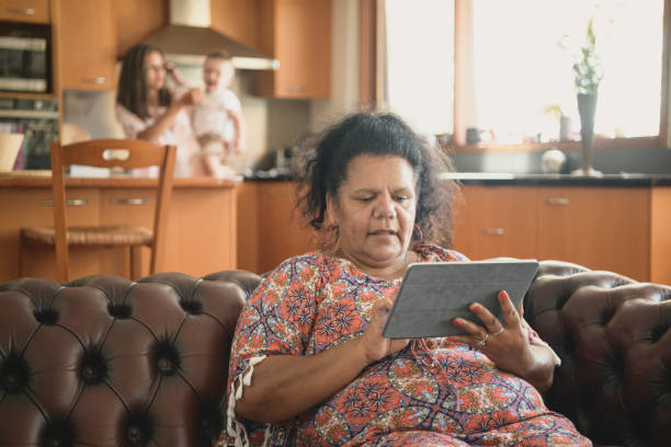 Mature woman at home using digital tablet Aboriginal woman in her 50s sitting on leather sofa and surfing the internet aborigine woman stock pictures, royalty-free photos & images