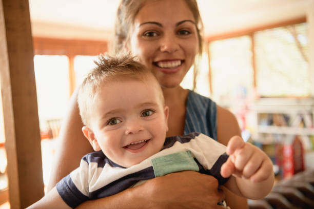 mujer alegre celebración a joven hijo y sonriendo a la cámara de - babies and children close up horizontal looking at camera fotografías e imágenes de stock