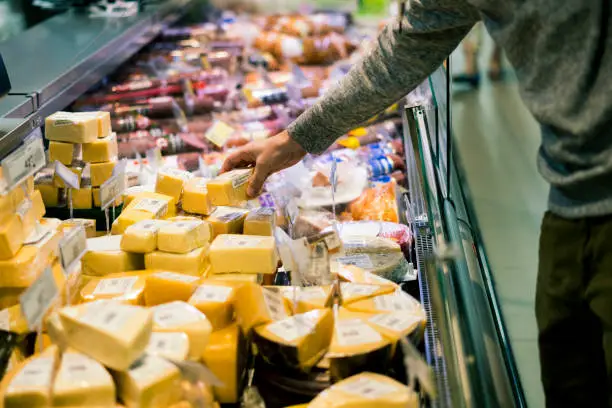 Photo of close up person choosing cheese in the food shop