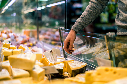 close up person choosing piece of  cheese in food shop