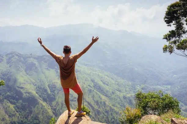 Man standing with raised hands on the top of Ella rock peak. Sri Lanka