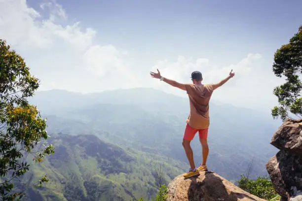 Hiker standing on a peak of mountain with raised hands. Ella rock. Sri Lanka