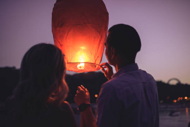 istock rear view of young couple launching sky lantern on river beach in evening 1030723952
