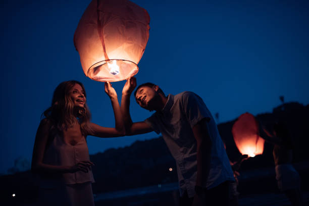 istock young couple looking at sky lantern on river beach in evening 1030724488