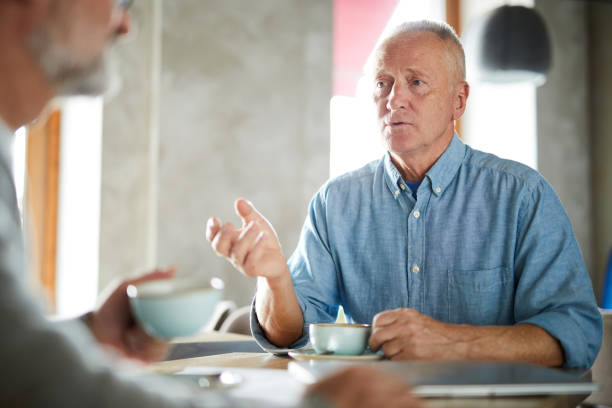 istock Confident handsome senior man in casual shirt gesturing hand while sharing his thoughts with friend, they drinking coffee in cafe 1030725680