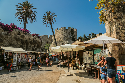 Rhodes, Greece – August 29, 2018: Wall and park in a trench around Fortress with market stalls for tourist souvenirs.