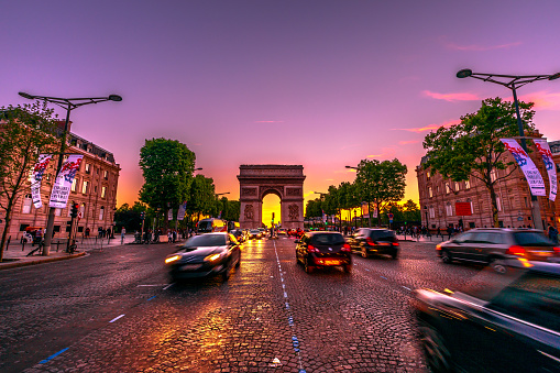 Paris, France - July 2, 2017: Avenue des Champs Elysees and iconic Arc de Triomphe at twilight with traffic street. Arch of Triumph in a colorful sunset sky.