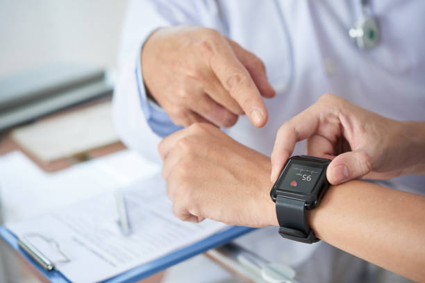 Crop patient showing heart rate to doctor Hands of anonymous patient using fitness tracker to show medical practitioner hear rate during checkup in doctor's office fitness tracker photos stock pictures, royalty-free photos & images