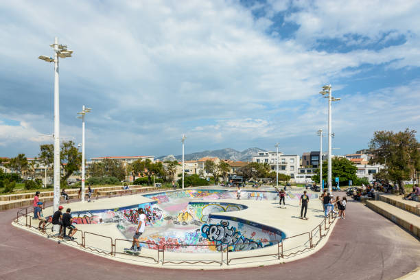 gesamtansicht von der skate-bowl von marseille, frankreich, bekannt als der skatepark von prado, mit jungen menschen, skaten, rollerskating oder roller von einem sonnigen nachmittag bei bewölktem himmel. - skateboard park ramp skateboard graffiti stock-fotos und bilder