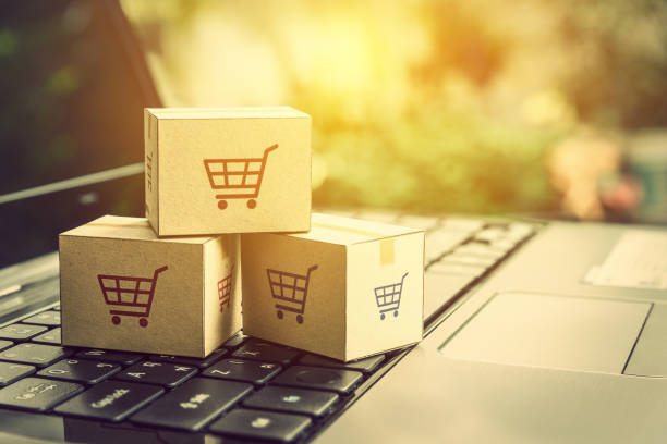 Online shopping / ecommerce and delivery service concept : Paper cartons with a shopping cart or trolley logo on a laptop keyboard, depicts customers order things from retailer sites via the internet. compras en línea / concepto de servicio de comercio electrónico y entrega: papel cajas de cartón con un carrito de compras o logo de la carretilla en un teclado de ordenador portátil, representa cosas de orden de los clientes de sitios de minorista a t
