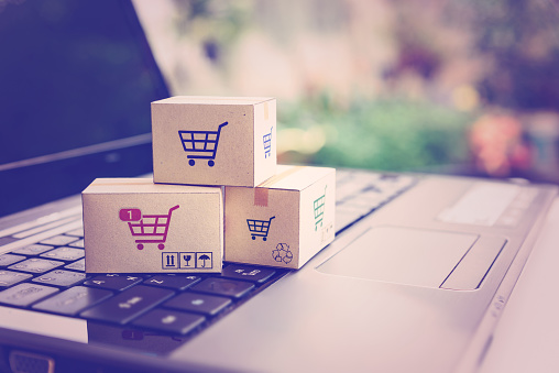 Online shopping / ecommerce and delivery service concept : Paper cartons with a shopping cart or trolley logo on a laptop keyboard, depicts customers order things from retailer sites via the internet.