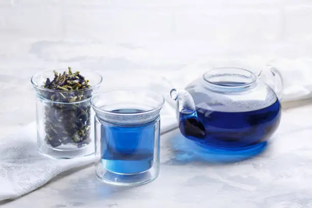 Photo of Butterfly pea flower tea is brewed in a glass teapot and served into a transparent cup. Blue herbal tea.