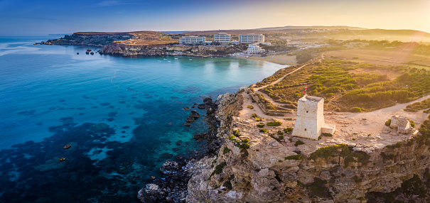 Ghajn Tuffieha, Malta - Aerial panoramic view of the coast of Ghajn Tuffieha with Watch Tower, Golden Bay beach and crystal clear sea water at sunrise