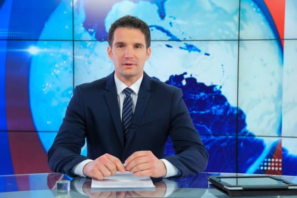 Man sitting in news studio. Ready to go live. Some papers and digital tablet on his desk.